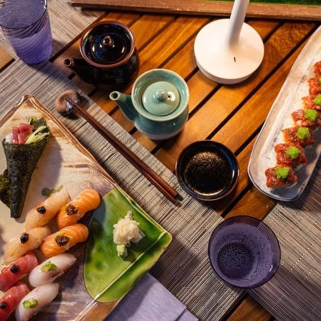 Artfully arranged sushi platter with nigiri, hand rolls, and sauces set on a wooden outdoor table under warm ambient lighting.